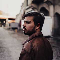 Homme barbu pensif en veste cuir dans ruelle urbaine, style mobilier-design-pierre-aveyron en Aveyron