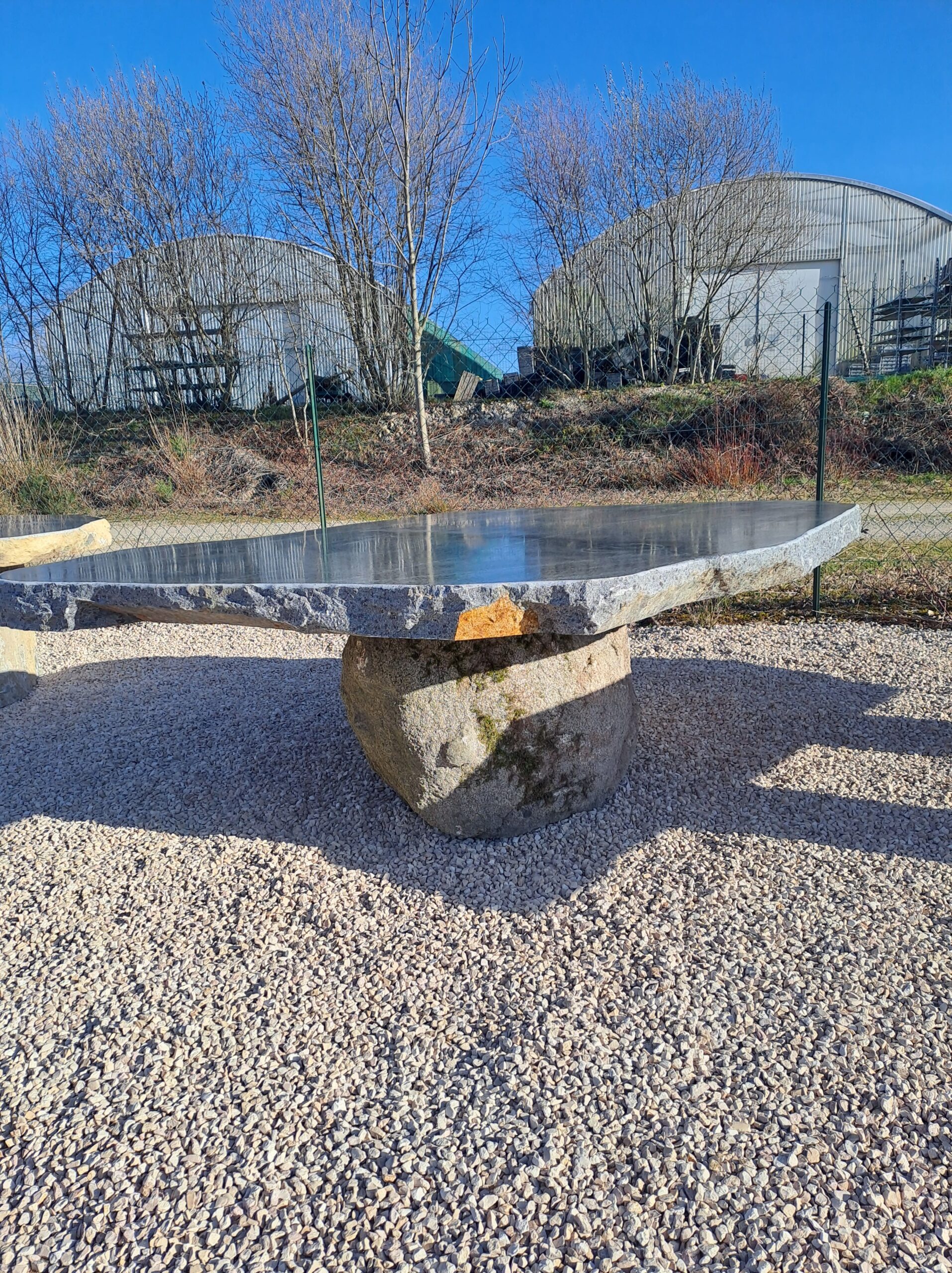 Table de jardin en pierre brute mobilier-design-pierre-aveyron dans un paysage rural ensoleillé en Aveyron