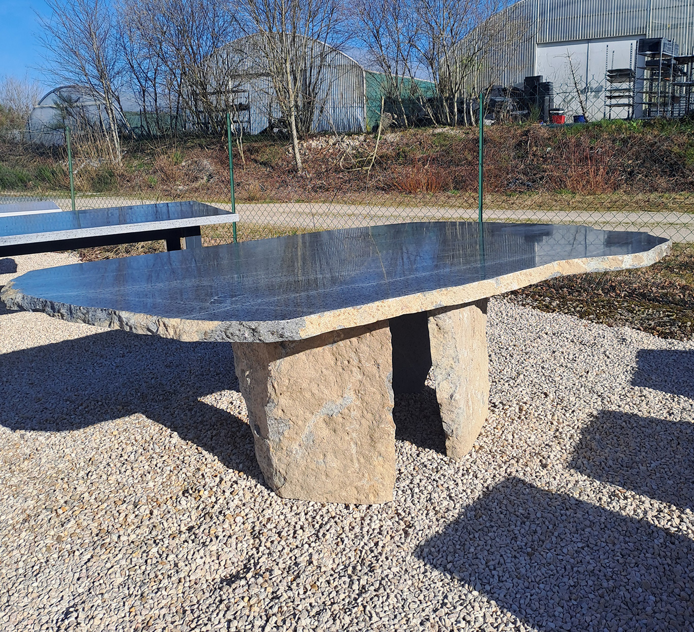 Grande table en pierre brute sur gravier, création mobilier-design-pierre-aveyron en extérieur rural ensoleillé en Aveyron