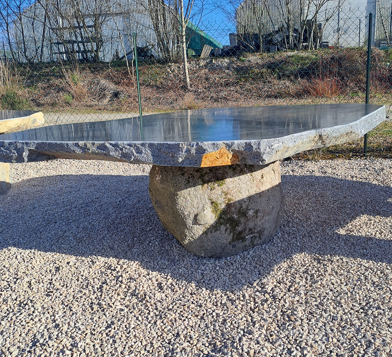 Table de jardin en pierre brute mobilier-design-pierre-aveyron dans une cour en gravier en Aveyron